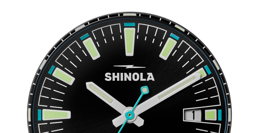 Black dial, luminous markers, turquoise accents.