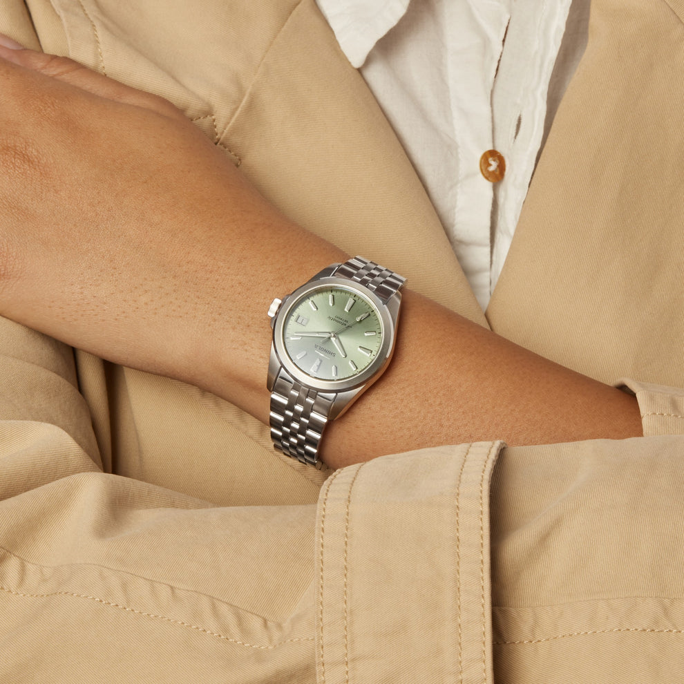 Green dial stainless steel watch on wrist.