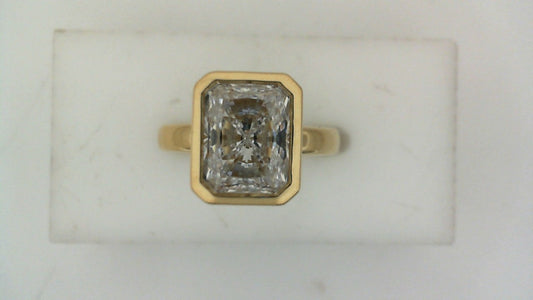 Front view of a yellow gold engagement ring featuring a rectangular-cut diamond in a bezel setting.