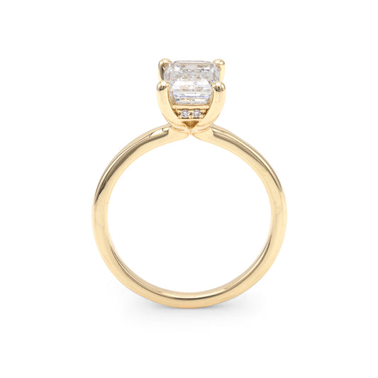Side profile of a yellow gold solitaire engagement ring featuring an emerald-cut center diamond in a four-prong setting with a hidden diamond halo.