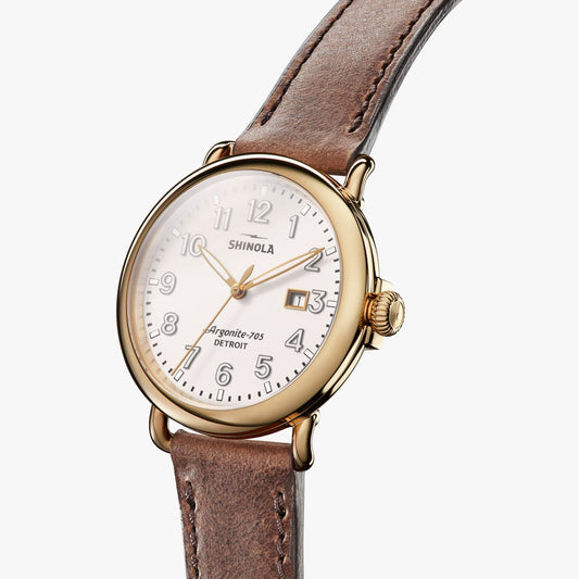 Gold-tone watch with white dial, leather strap.